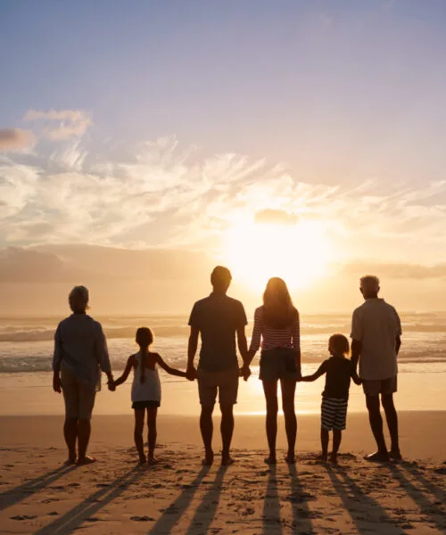 Rear View Of Multi Generation Family Silhouetted On Beach